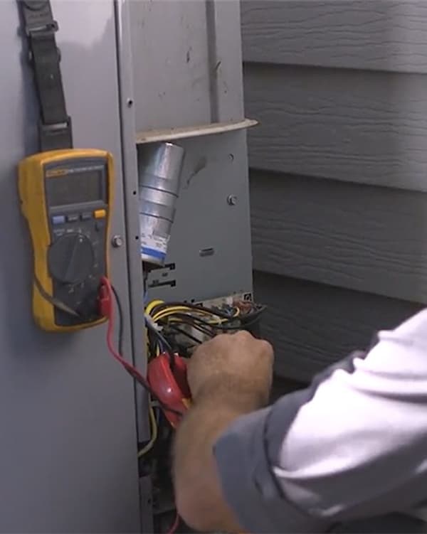 R&W technician testing the wiring inside an outdoor AC condenser